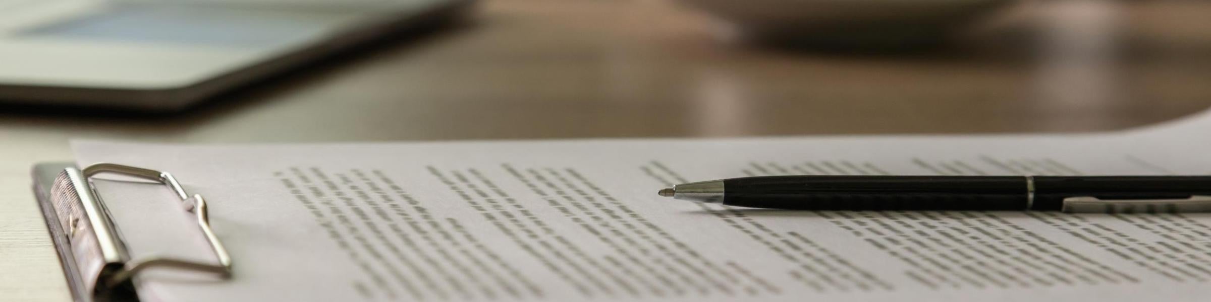 A clipboard of papers setting on a desk with a black pen resting on top